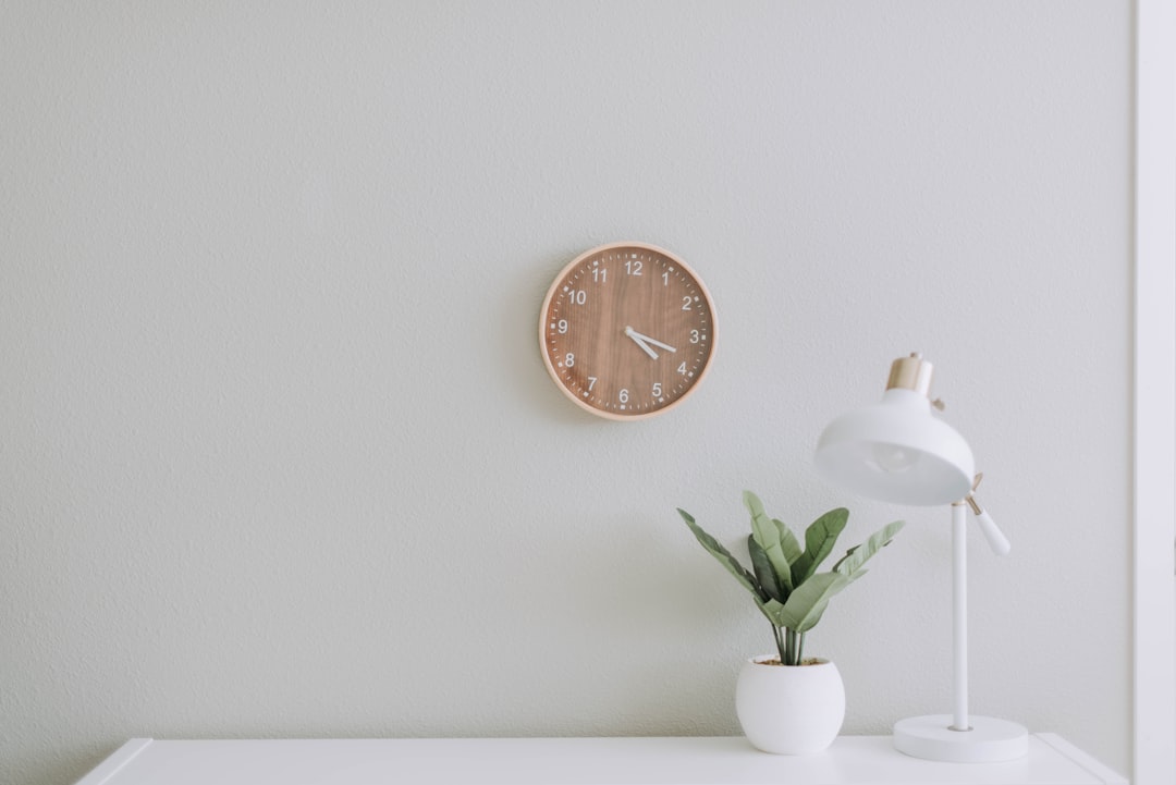 Minimalist home office desk with white lamp, small plant, and wooden wall clock